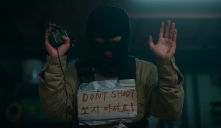 Um assassino mascarado com uma placa escrita DON'T SHOOT em A Shop for Killers