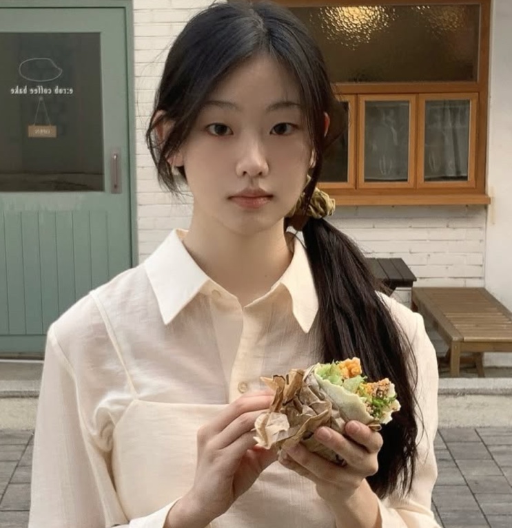 Seo Su-min segurando um sanduíche em frente a um café