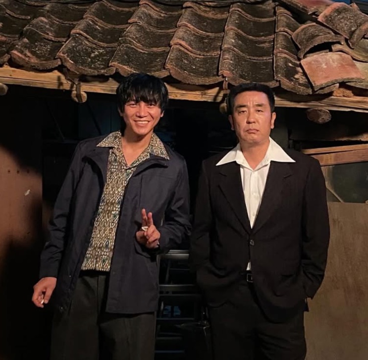 Won Hyun-jun de terno, nos bastidores de uma gravação