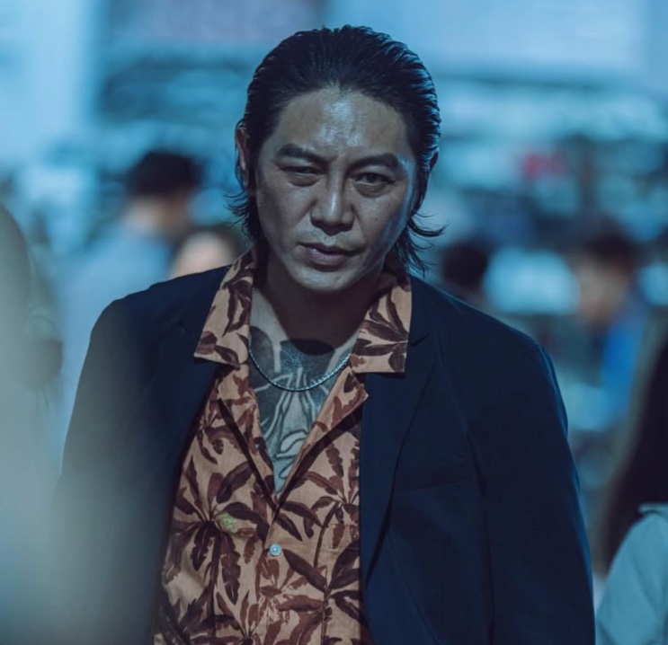 Won Hyun-jun com visual de yakuza, camisa estampada e tatuagem