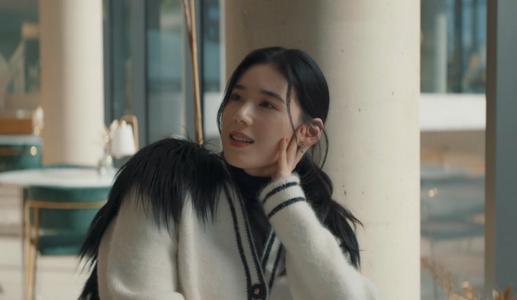Jung Eun-chae de casaco de pelos, sentada em um café, com a mão no rosto