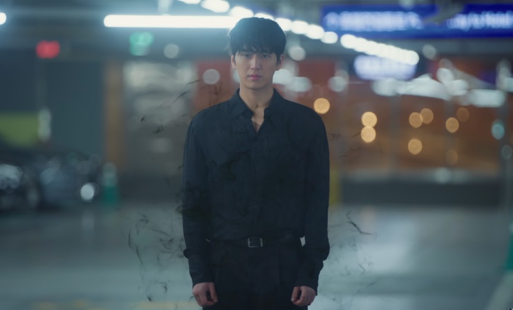Ji-hwan em pé no estacionamento, com fumaça ao redor