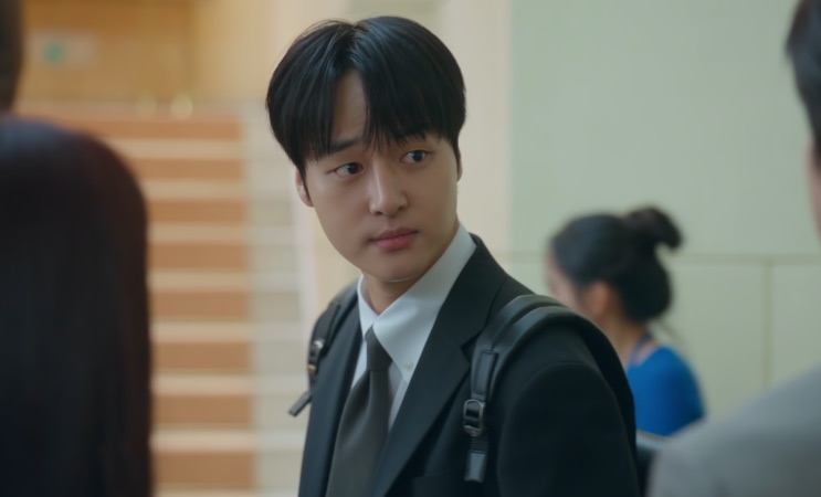 Ji-hwan de terno e mochila num corredor