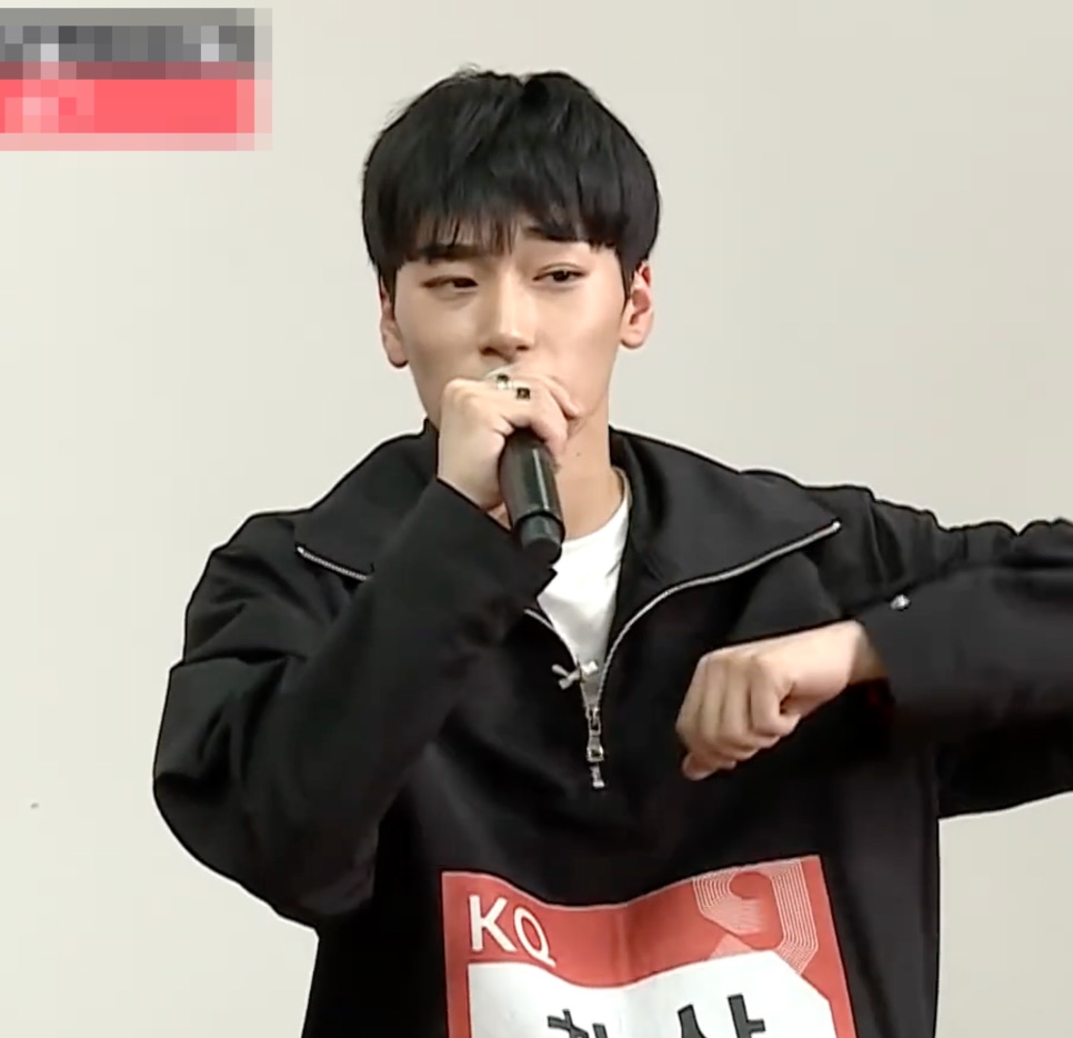 Choi San bem jovem cantando ao microfone, com um crachá da KQ na roupa