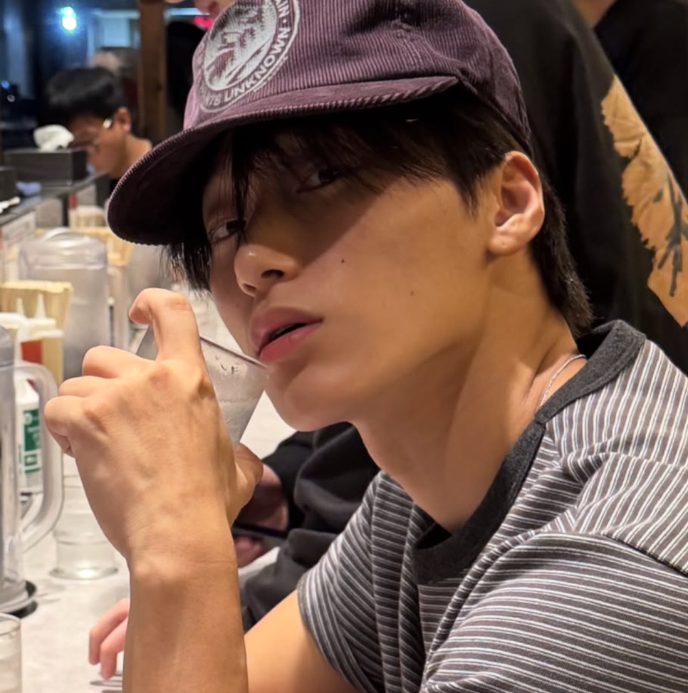 Choi San de boné e camiseta listrada, tomando uma bebida num restaurante