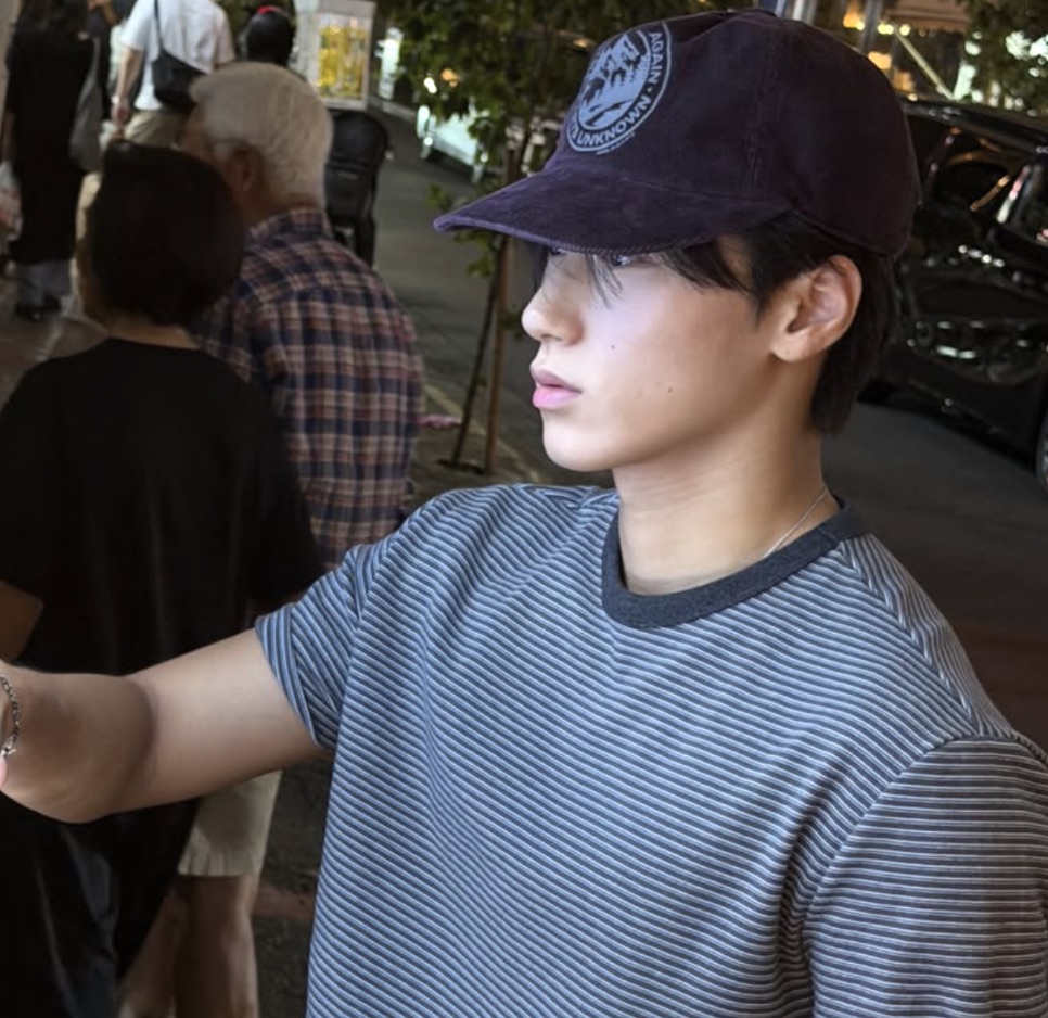 Choi San de boné e camiseta listrada, de perfil, numa rua à noite
