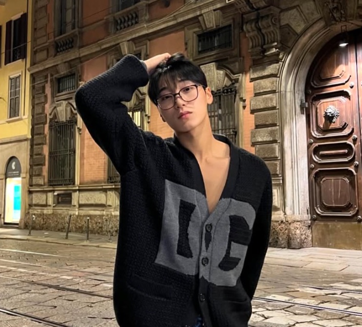 Choi San numa rua da Europa, de cardigã, passando a mão no cabelo