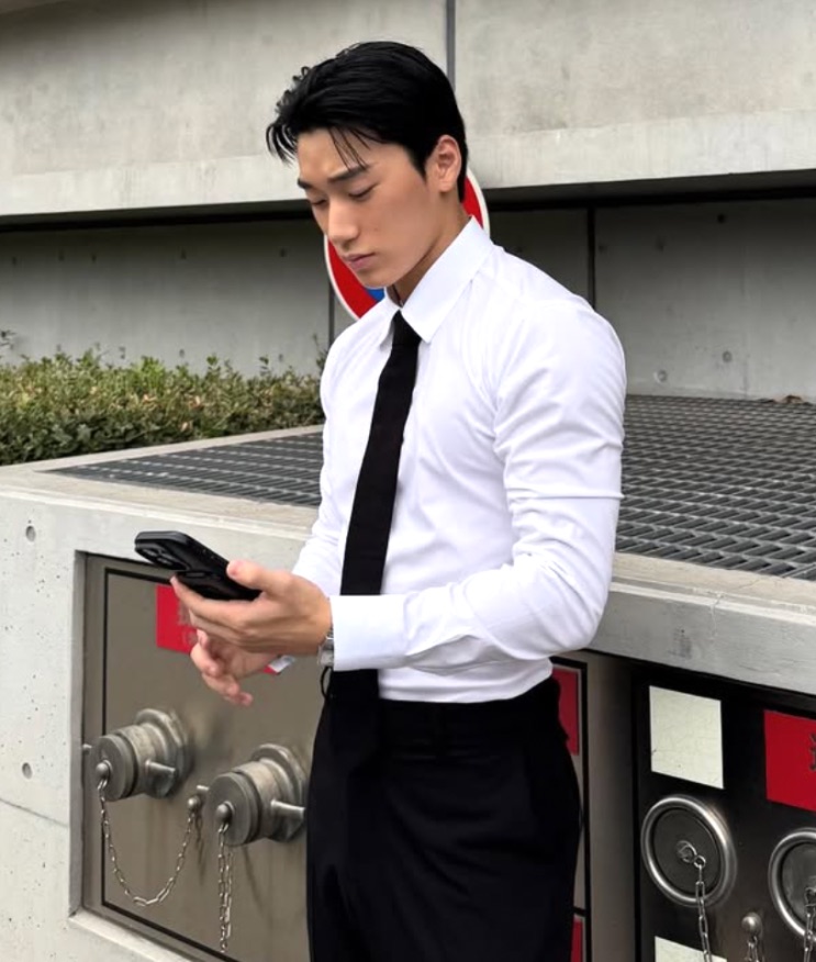Choi San atual, de camisa branca e gravata, mexendo no celular