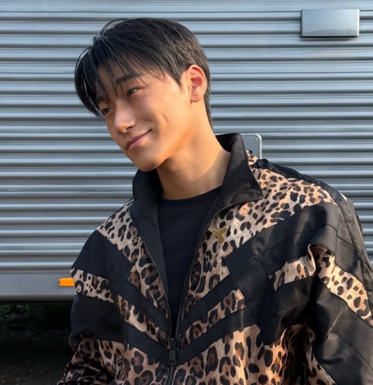 Choi San atual sorrindo, de jaqueta com estampa de onça