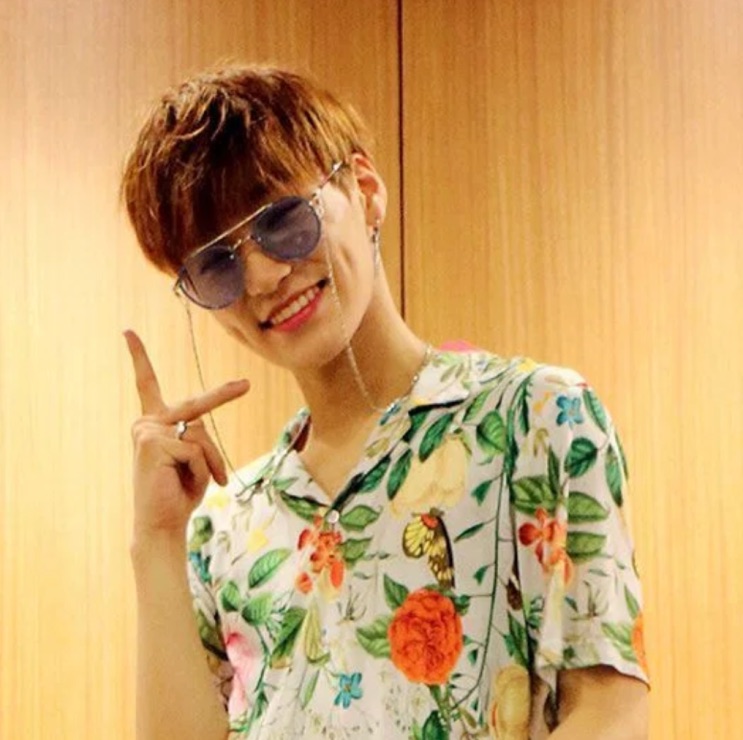 Choi San na época do debut, de camisa florida e óculos escuros, bem mais magro