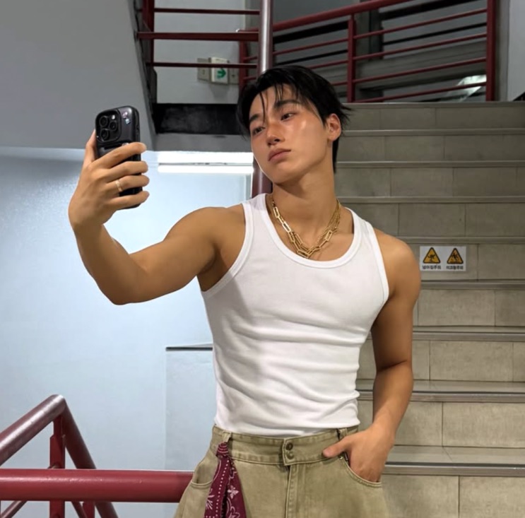 Selfie atual de Choi San no espelho da escada, de regata branca, braços definidos