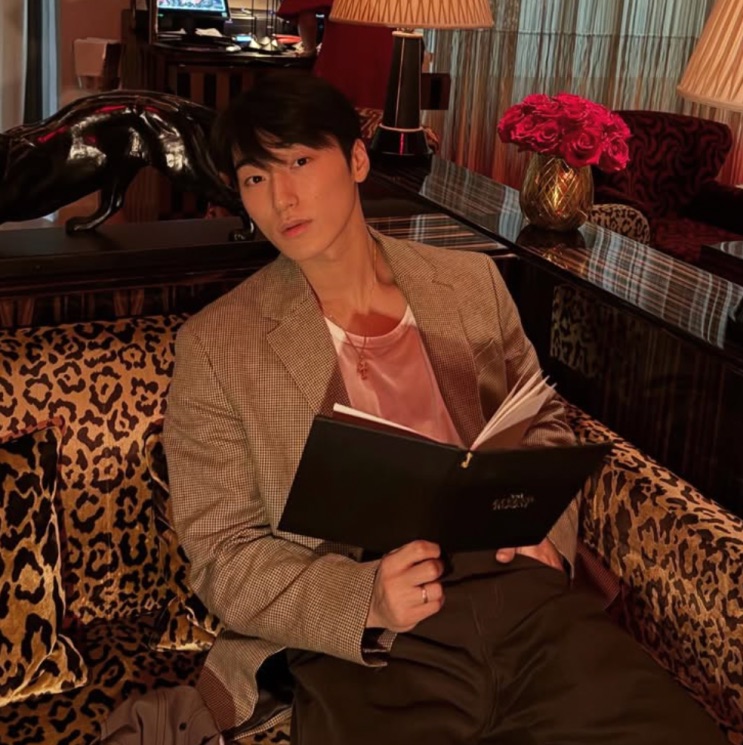 Choi San atual, de blazer, sentado lendo um caderno