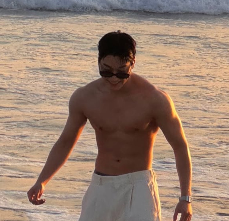 Choi San atual sem camisa na praia, mostrando o abdômen definido