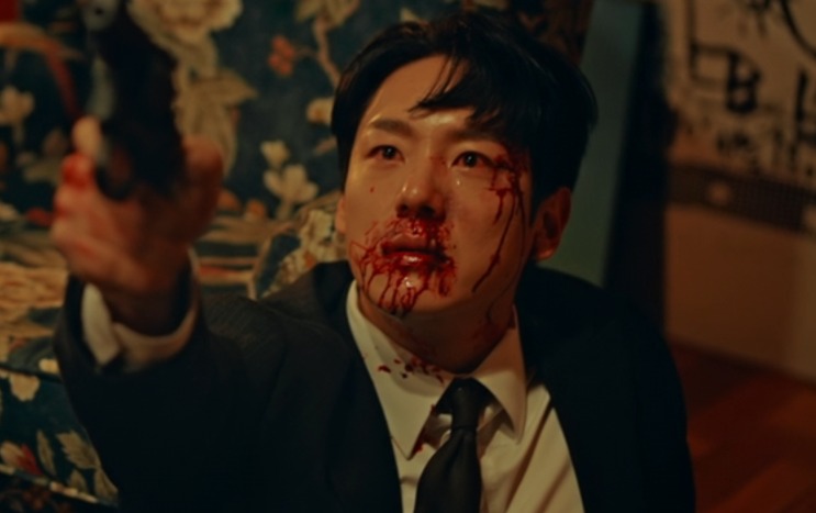 Jin Seung-joo caído no chão, ensanguentado, apontando uma arma