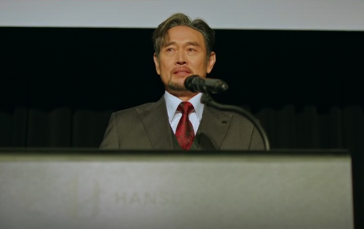 Um executivo de terno no púlpito da Hansu, diante do microfone