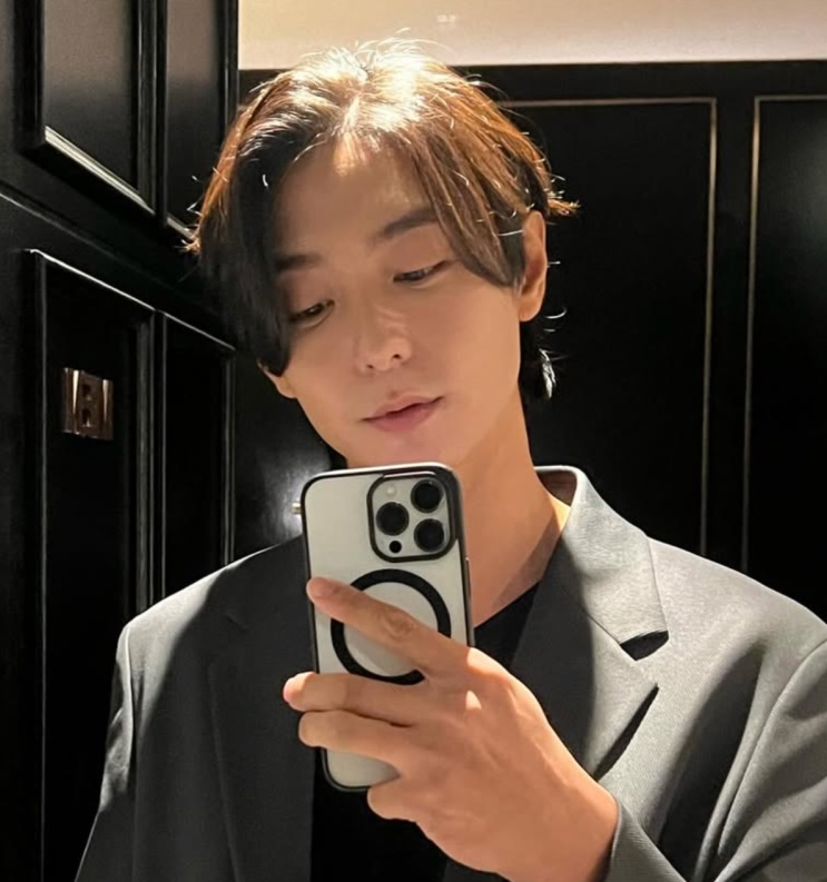 Hyun Woo de blazer, tirando uma selfie no espelho do elevador