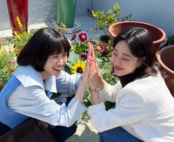 Ha Yoon-kyoung com uma amiga, sorrindo, diante de girassóis