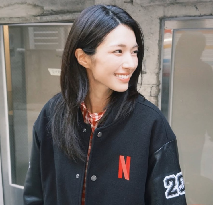 Ha Young sorrindo, de jaqueta com o logo da Netflix