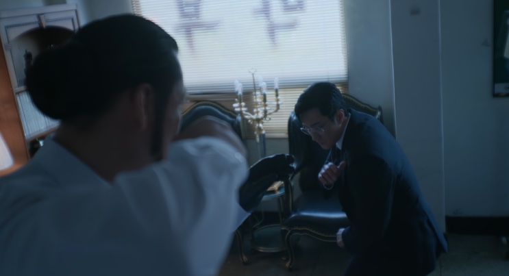 Um braço enorme de camisa branca partindo pra cima do Kim, que se agacha em posição de defesa