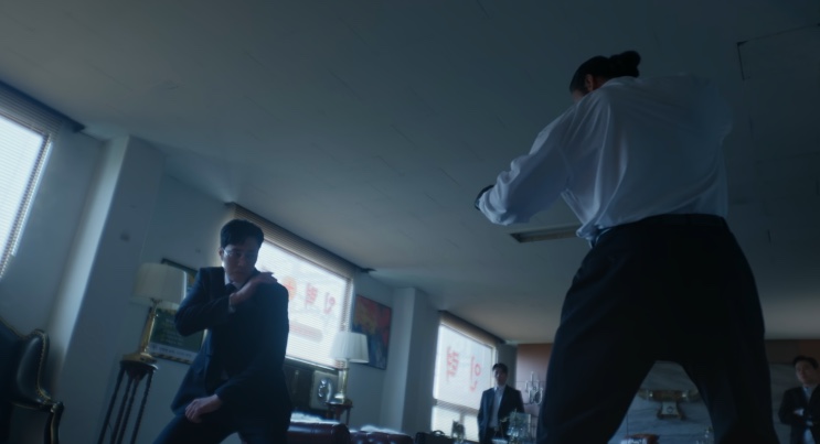 O Lee Do-gyu de camisa branca, de costas pra câmera, encarando o Kim do outro lado da sala