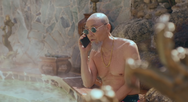 Jo Pyeong-gyeon, um senhor careca de óculos escuros redondos e barbicha branca, atendendo o celular dentro de uma banheira de água quente