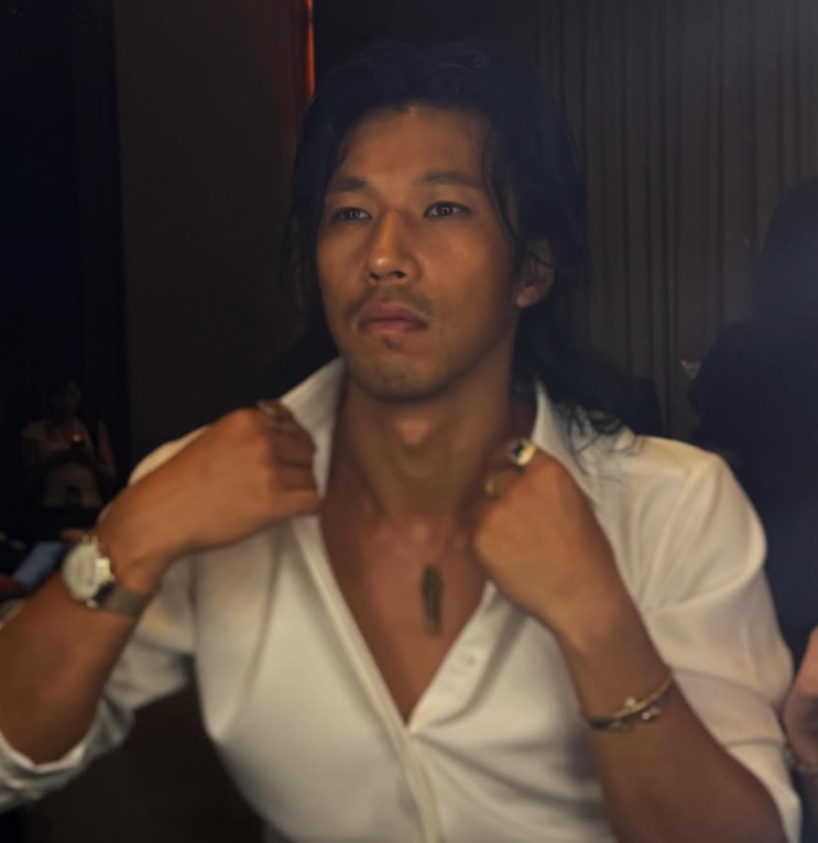 Kim Min de camisa branca, ajeitando a gola, num evento noturno