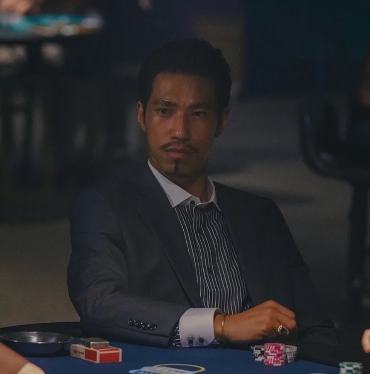 Kim Min de terno, sentado à mesa de carteado, como o John em A Próxima Aposta