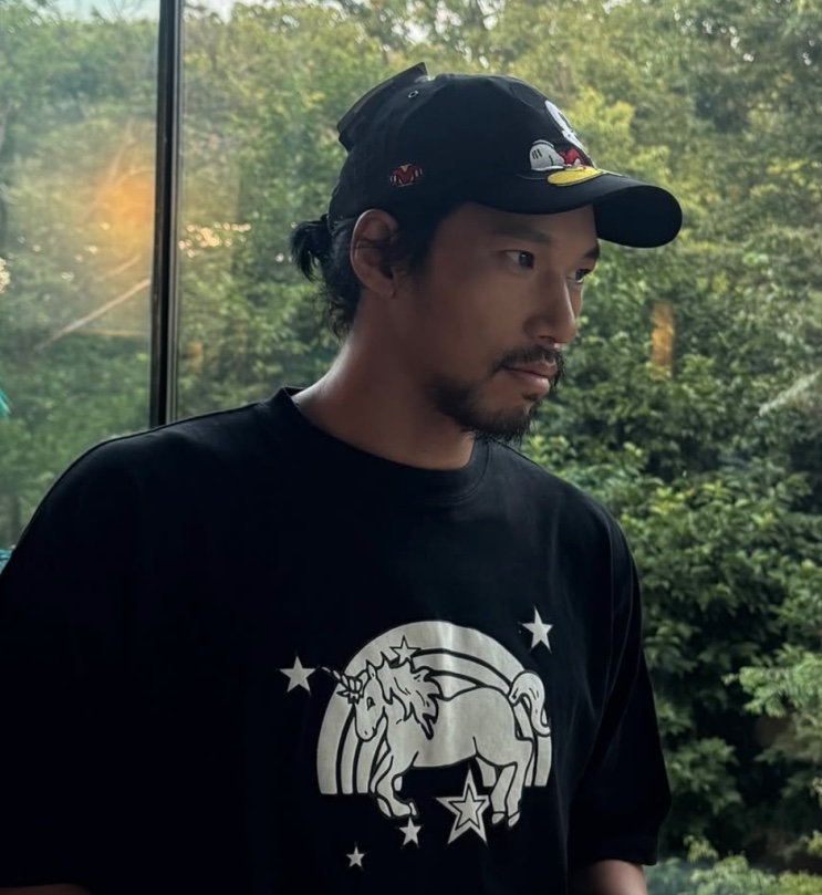 Kim Min de boné e camiseta preta, de perfil, em foto recente