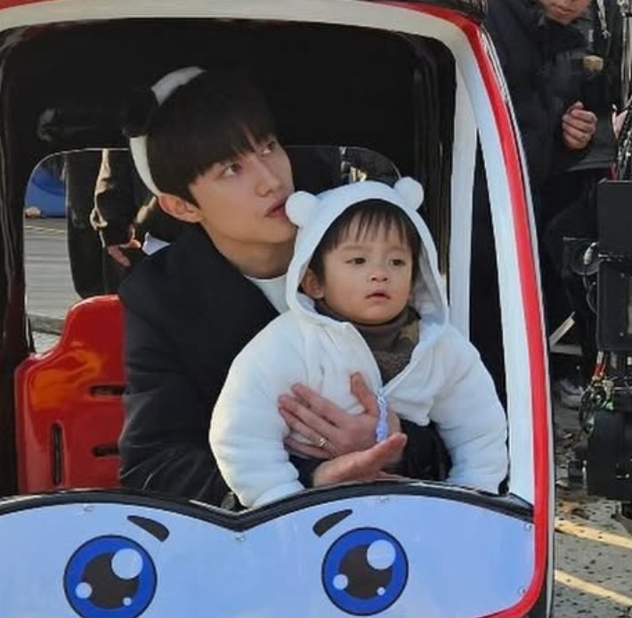 Hong Soo-cheol com o bebê num brinquedo em Rainha das Lágrimas