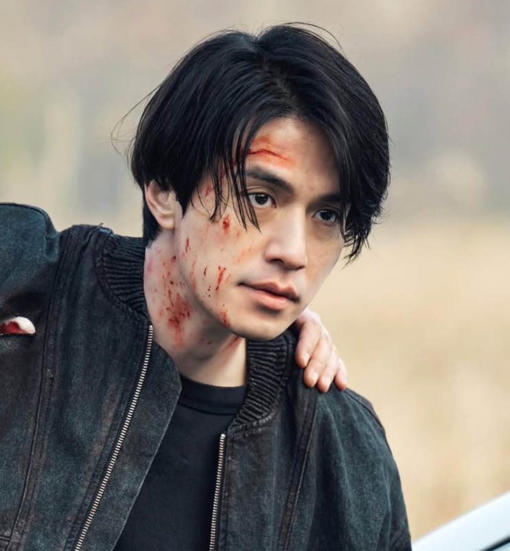 Lee Dong-wook com o rosto marcado de sangue, de jaqueta preta
