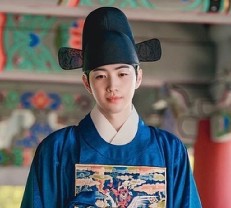 Kang Hoon de traje azul e chapéu da corte, em cena de dorama de época