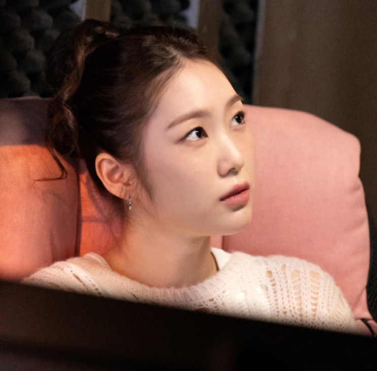 Myeong Tae-geum recostada num sofá rosa, de suéter claro, olhando para o lado