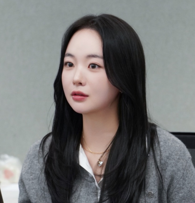 Kim Chae-eun de cardigã cinza e colar dourado, olhando para o lado
