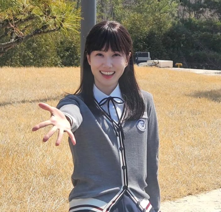 Park Eun-bin de uniforme escolar, sorrindo com a mão estendida para a câmera