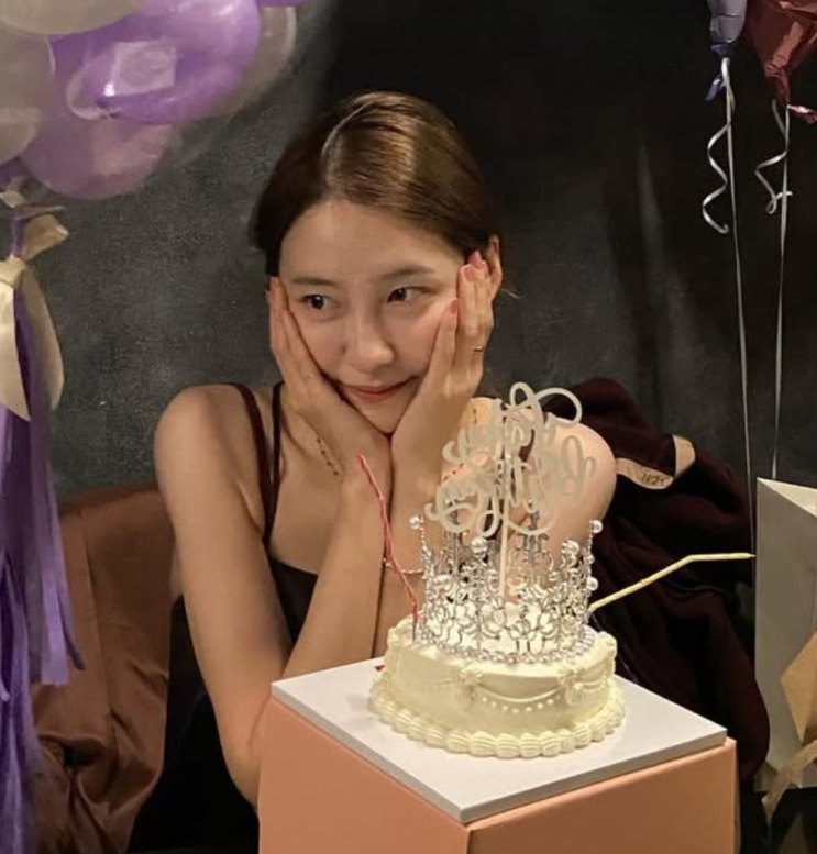 Park Ji-hyun com as mãos no rosto, diante de um bolo de aniversário