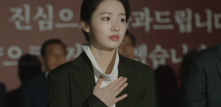 Jin Ye-jun de terno escuro, com a mão sobre o peito, durante um pedido público de desculpas