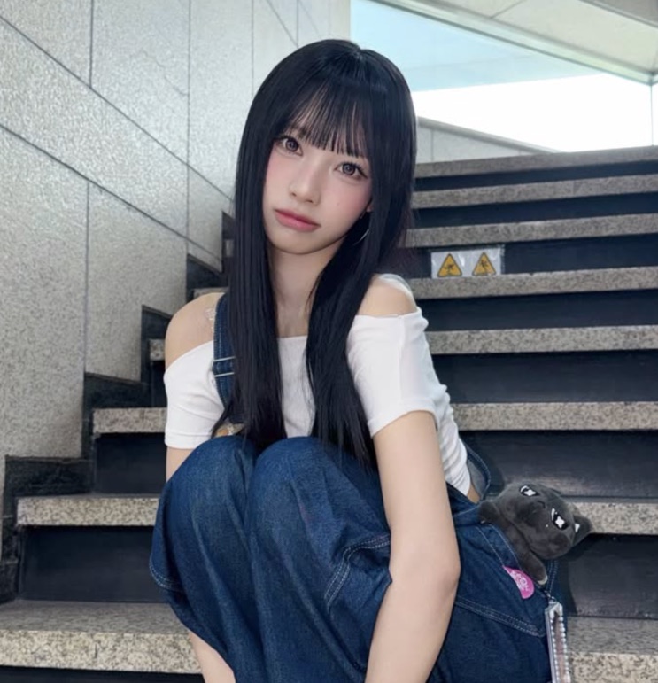 Woni sentada numa escada, de top branco e calça jeans