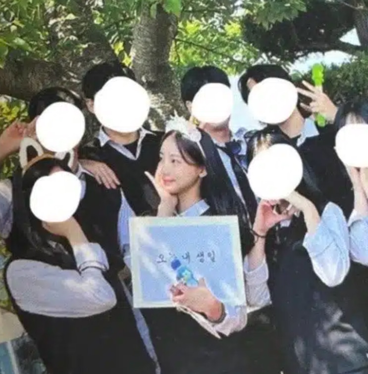 Woni na formatura, cercada de colegas com os rostos apagados, segurando um cartaz