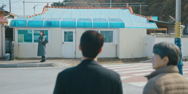 Ji-yoon parada do outro lado da rua, diante de uma casa de telhado azul