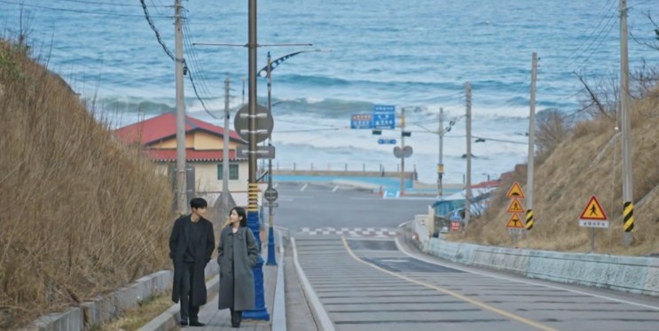 Si-woo e Ji-yoon conversando na calçada, com a descida e o mar ao fundo