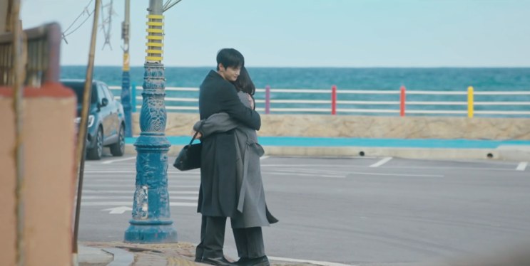 Si-woo e Ji-yoon se abraçando no cruzamento, com o mar atrás