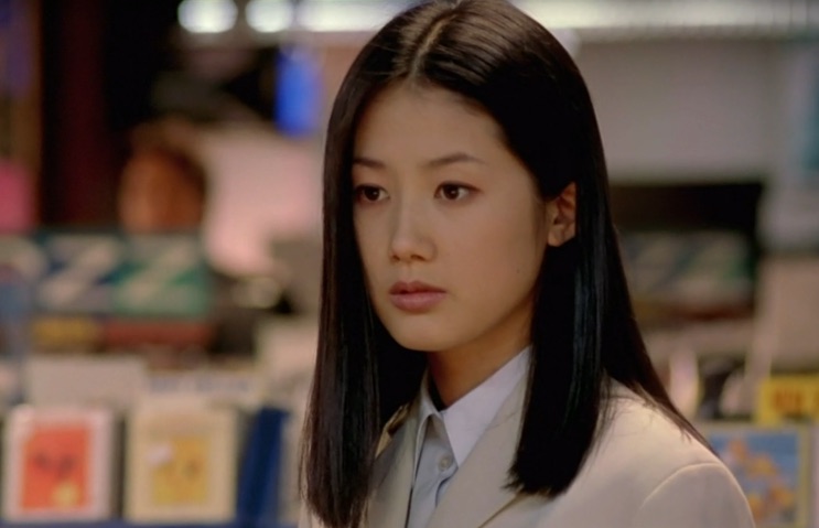 Shim Eun-ha em pé numa loja, com prateleiras coloridas atrás