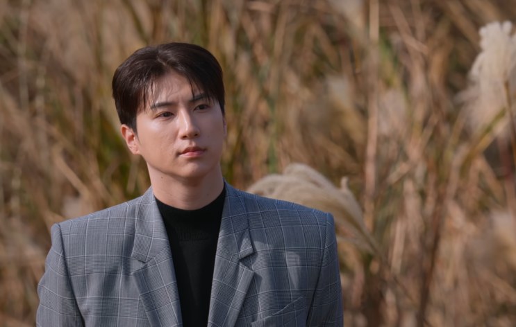 Choi Hyuk-joon de terno, em pé no meio do capim prateado