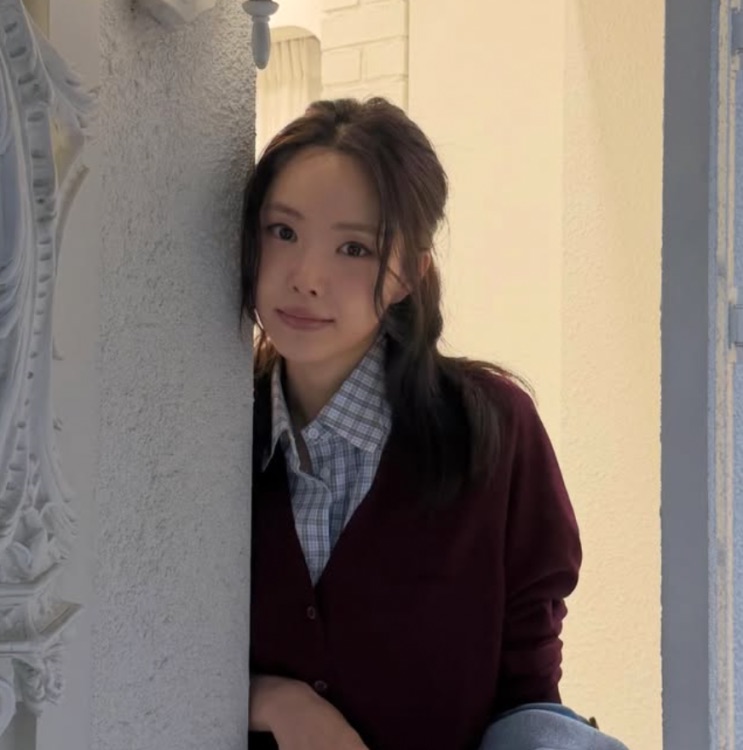 Son Na-eun de cardigã vinho, encostada numa coluna