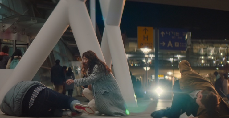 Da-eun agachada no chão do aeroporto ao lado de duas pessoas caídas em Sweet & Sour