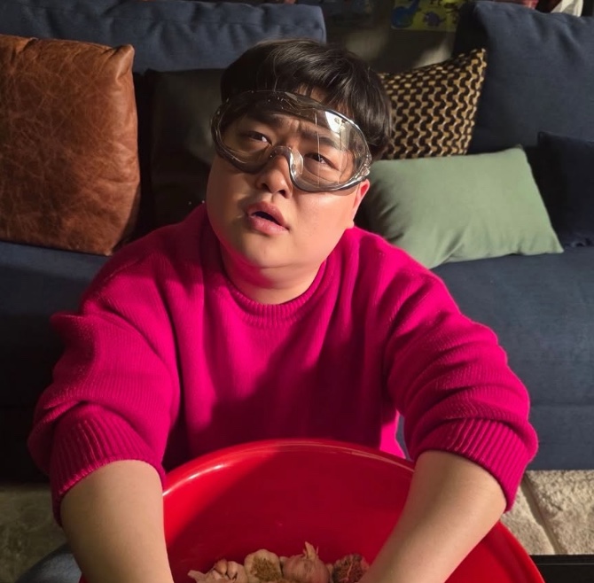 Kim Kyu-won de suéter rosa e óculos de natação, segurando uma bacia vermelha