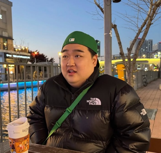 Kim Kyu-won na rua, de casaco de inverno, segurando um copo de café