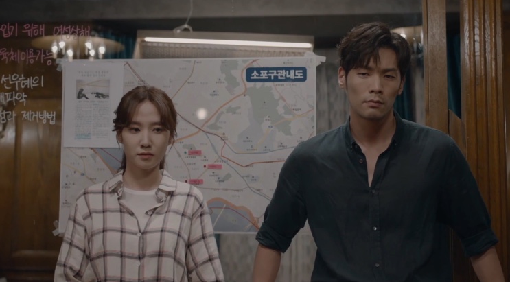 Jung Yeo-wool e Lee Da-il de pé no escritório de detetives, diante de um mapa na parede