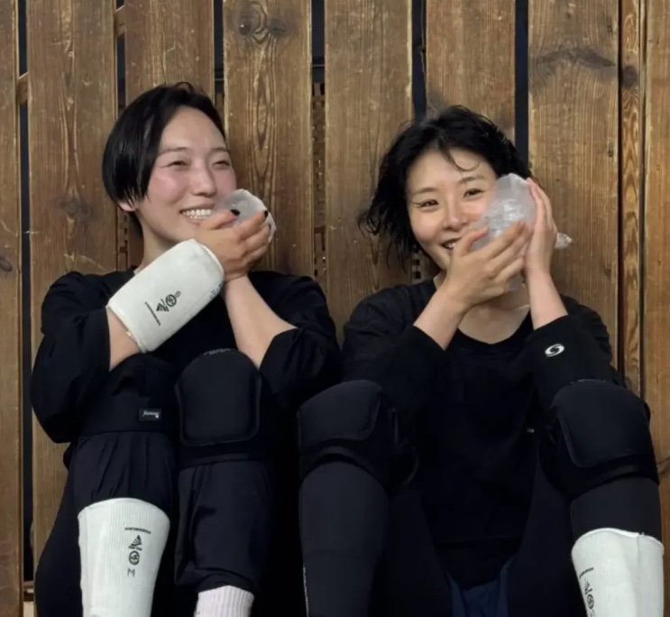 Hyunri e outra pessoa em treino de ação, com joelheiras e proteções
