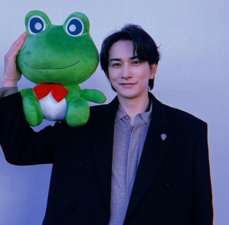 Machida Keita num evento, segurando um boneco de sapo verde